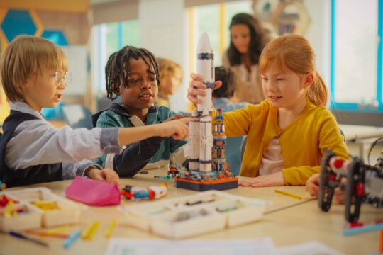 Students sit at a table, building a rocket as part of a STEM lesson.