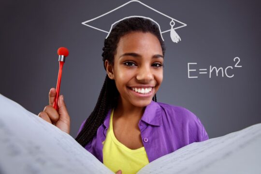 A smiling student stands in front of a chalkboard with a math problem written on it.