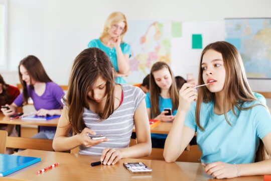 Distracted students talk and play on their phones, not listening to the teacher.