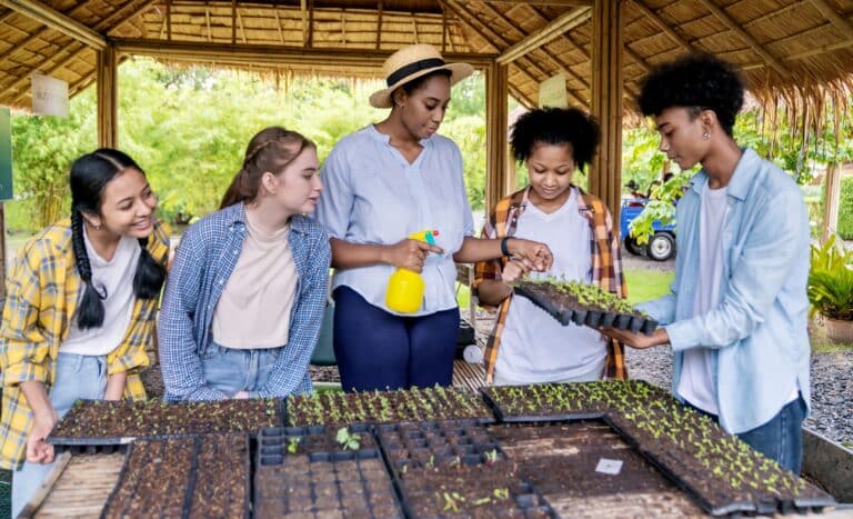 A group of students standing with their teacher, learning about plants on a farm.