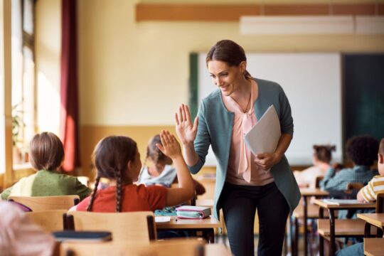 A teacher high fives her student as she collects their papers.