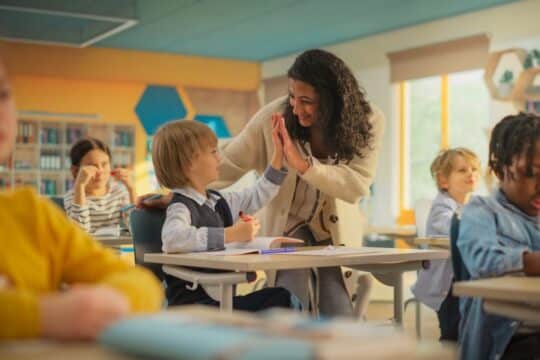 A teacher and student high-five in the classroom.