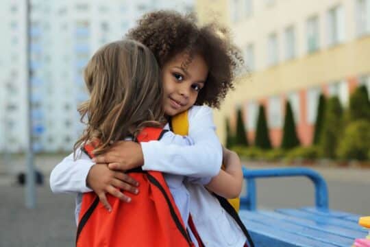 Two young students hug outside of their school building.