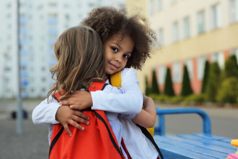 Two young students hug outside of their school building.