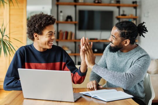 A father and son work on completing homework together at the kitchen table and high five.
