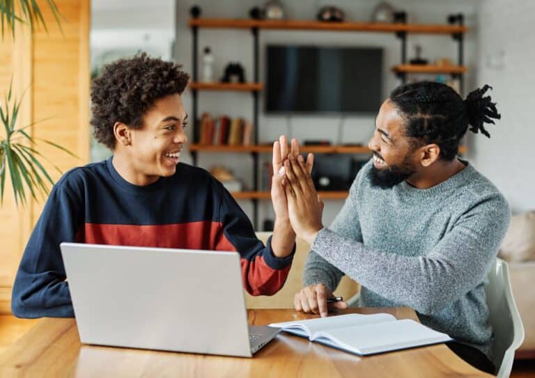 A father and son work on completing homework together at the kitchen table and high five.