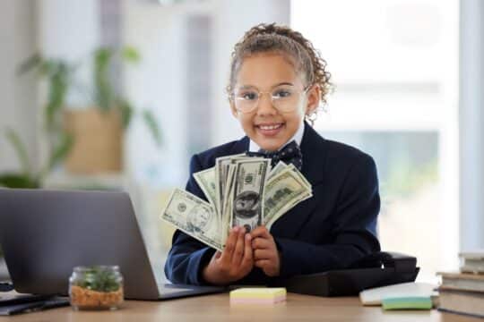 A young girl sits in a suit and fans out her paper money.