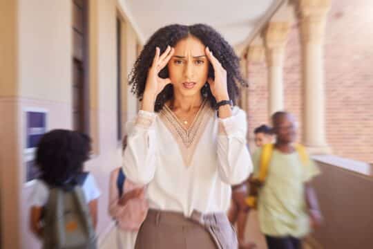 A teacher walks down the hallway, holding her hands to her head, looking incredibly stressed.
