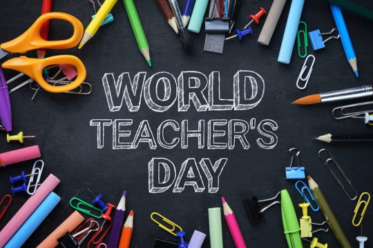 World Teachers Day is written on a chalkboard with school stationary surrounding it.
