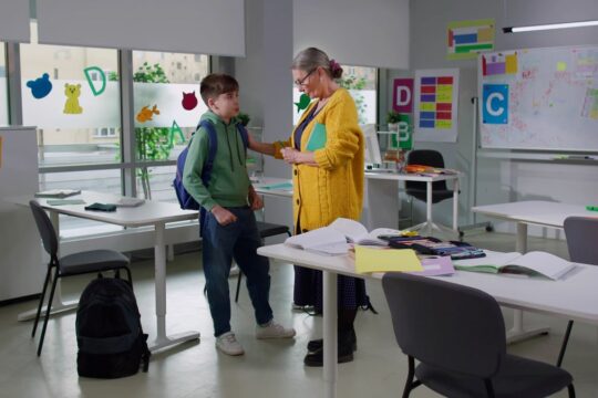 A teacher stands with her student after class, privately talking.