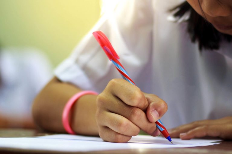 Young student writing on paper while sitting at a desk.